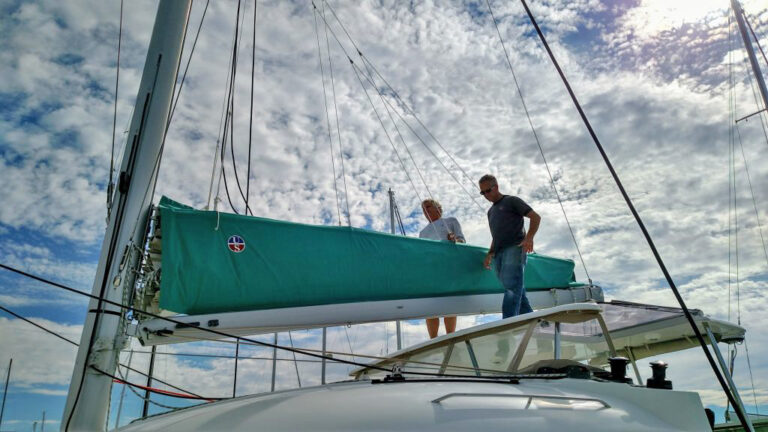 Sailors standing next to a green stack pack boom cover supported by lazy jacks on a catamaran