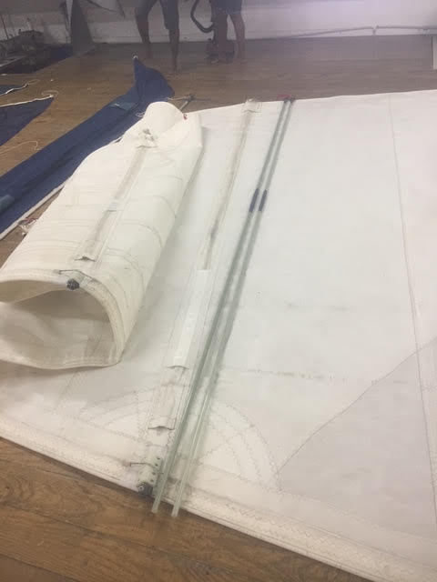 White sail laid out with battens during inspection and repair, an important step in off-season sail storage.